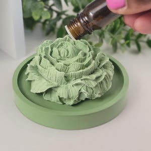 May include: A green ceramic rose diffuser with a round base. Essential oil is being dripped onto the rose.