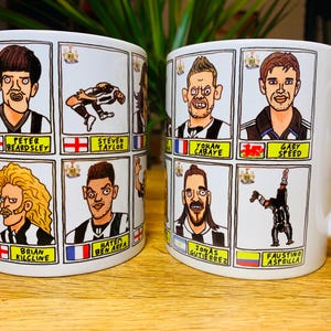 Peut inclure: Deux tasses en c&eacute;ramique blanche avec des illustrations en noir et blanc de joueurs de football. Chaque tasse pr&eacute;sente un joueur diff&eacute;rent avec son nom et son &eacute;quipe imprim&eacute;s en dessous. Les tasses sont sur une surface en bois.