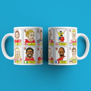 May include: Two white mugs with cartoon illustrations of soccer players. The mugs feature a red and white color scheme with the names of the players printed below each illustration. The mugs are on a blue background.