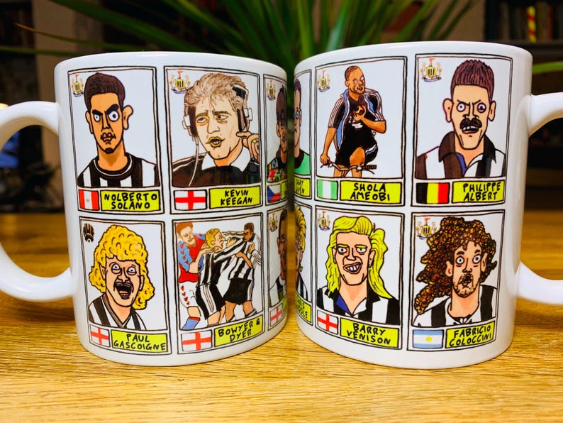 Peut inclure: Deux tasses en c&eacute;ramique blanche avec des poign&eacute;es noires. Chaque tasse pr&eacute;sente une grille de neuf illustrations de joueurs de football en dessin anim&eacute; avec leurs noms en dessous. Les tasses sont sur une surface en bois.