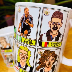 Peut inclure: Une tasse en c&eacute;ramique blanche avec une illustration de joueurs de football en dessin anim&eacute;. La tasse pr&eacute;sente les noms "Shola Ameobi", "Barry Venison", "Philippe Albert" et "Fabricio Coloccini".