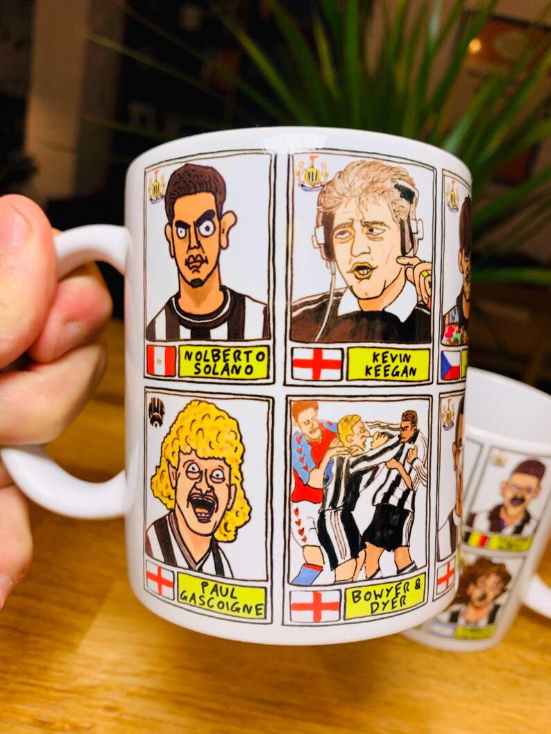 Peut inclure: Une tasse en c&eacute;ramique blanche avec une illustration de joueurs de football en dessin anim&eacute;. La tasse pr&eacute;sente quatre joueurs diff&eacute;rents, dont Nolberto Solano, Kevin Keegan, Paul Gascoigne et Bowyer & Dyer. La tasse a une poign&eacute;e noire et un int&eacute;rieur blanc.