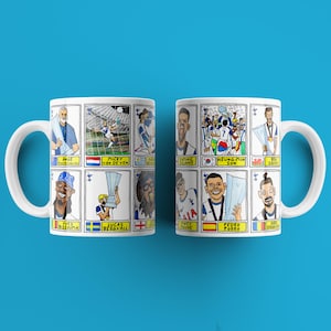 May include: Two white ceramic mugs with cartoon illustrations of soccer players and scenes. Each mug features a different set of images, with players' names and flags. The mugs have white handles and are set against a blue background.