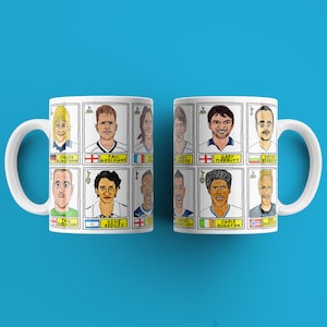 May include: Two white mugs with a cartoon illustration of soccer players. Each mug features 8 different players with their names and country flags. The mugs are on a blue background.