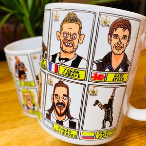 Peut inclure: Une tasse en c&eacute;ramique blanche avec des illustrations de joueurs de football en dessin anim&eacute;. La tasse porte les noms "Yohan Cabaye", "Gary Speed", "Jonas Gutierrez" et "Faustino Asprilla".