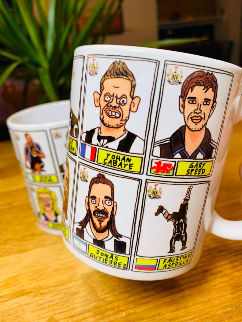 Peut inclure: Une tasse en c&eacute;ramique blanche avec des illustrations de joueurs de football en dessin anim&eacute;. La tasse porte les noms "Yohan Cabaye", "Gary Speed", "Jonas Gutierrez" et "Faustino Asprilla".