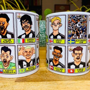 Puede incluir: Dos tazas de cer&aacute;mica blanca con ilustraciones de dibujos animados en blanco y negro de jugadores de f&uacute;tbol. Cada taza presenta un conjunto diferente de jugadores con sus nombres y nacionalidades impresos debajo de cada imagen.