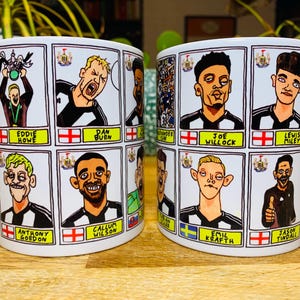 Puede incluir: Taza de cer&aacute;mica blanca con una ilustraci&oacute;n de dibujos animados en blanco y negro de los jugadores y el entrenador del Newcastle United Football Club. La taza presenta el escudo del equipo y los nombres de los jugadores y el entrenador.