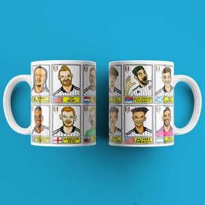 May include: Two white mugs with black and white illustrations of soccer players. Each mug features a different player with their name and country flag. The mugs are on a blue background.