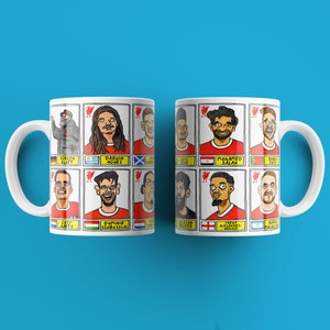 May include: Two white mugs with a comic book style design featuring the faces of Liverpool Football Club players. The mugs are printed with the names of the players, including "Darwin Nunez", "Mohamed Salah", and "Trent Alexander-Arnold".