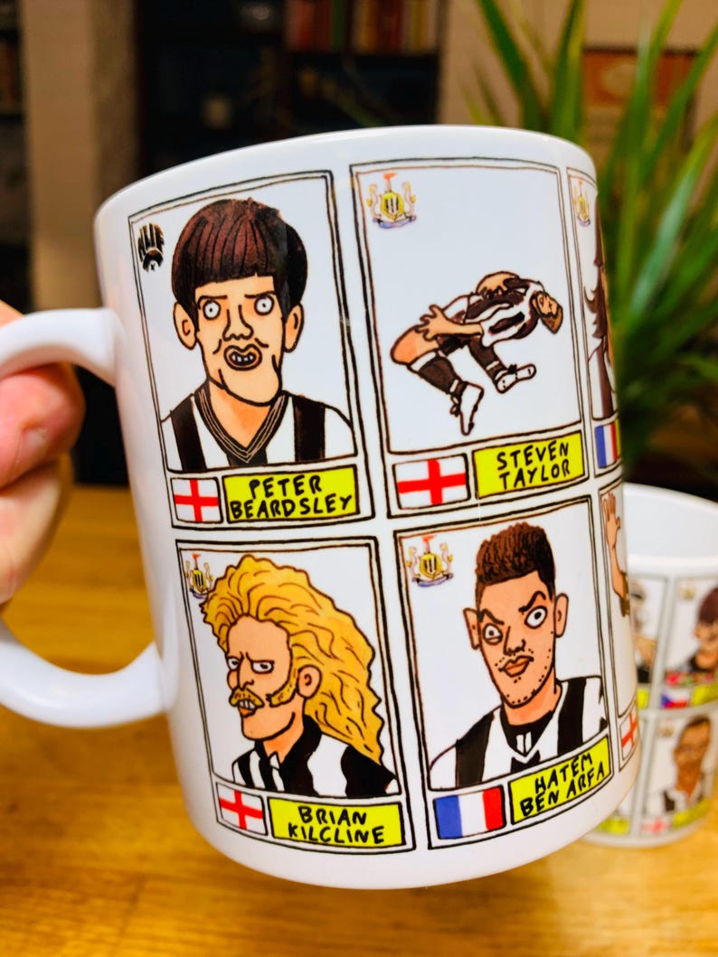 Peut inclure: Une tasse en c&eacute;ramique blanche avec des illustrations de joueurs de football en dessin anim&eacute;. Chaque joueur a un nom et un drapeau repr&eacute;sentant son pays d'origine. Les joueurs incluent Peter Beardsley, Steven Taylor, Brian Kilcline et Hatem Ben Arfa.