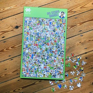 Op de afbeelding: Een groen omlijste legpuzzel met de woorden "NO SCORE DRAWS" en een cartoonafbeelding. De puzzel is gevuld met talrijke kleine afbeeldingen van mensen. Verschillende puzzelstukjes liggen verspreid rond de puzzel.