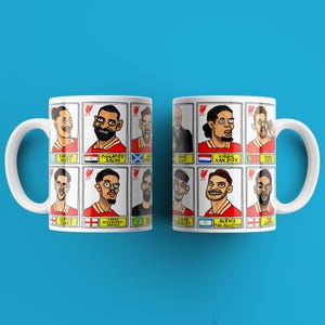 May include: Two white ceramic mugs with a red, white and blue design featuring cartoon illustrations of football players. The mugs have handles and are printed with the names of the players, including "Mohamed Salah", "Virgil van Dijk", and "Trent Alexander-Arnold".