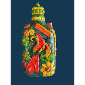 May include: A decorative bottle with a textured dark green surface featuring a relief design of a red and yellow parrot, orange flowers, and green foliage. The word HONDURAS is embossed in an orange banner. It has a matching stopper.