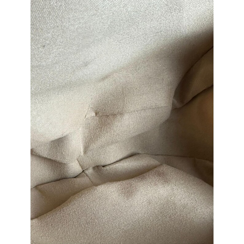 May include: Interior view of a beige fabric bag. The fabric has a textured appearance with visible seams and folds. The bag's interior is empty, showcasing the material's color and texture.