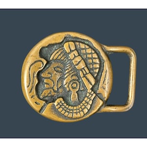 May include: A vintage brass belt buckle featuring a detailed relief of a Mayan figure in profile. The buckle has a rectangular frame and a circular central design with intricate carvings. The color is a warm, aged brass.