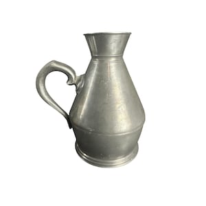 May include: A silver pewter pitcher with a rounded body and a handle. The pitcher has a wide mouth and a slightly flared lip.
