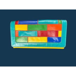May include: A rectangular wallet featuring a multi-coloured patchwork design made of leather segments in blue, yellow, green, red, and orange. The wallet is framed by a solid turquoise border and includes visible stitching along each colour block.