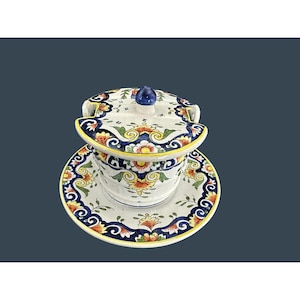 May include: A ceramic serving bowl with a lid and matching saucer. The bowl and lid are white with a blue, yellow, and orange floral design. The lid has a blue knob handle. The saucer has a matching design.