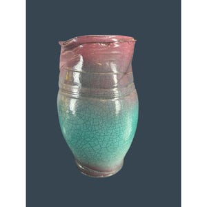 Könnte beinhalten: Handgefertigte Keramikvase mit Craquelé-Glasur. Die Vase wechselt von einem türkisfarbenen Sockel zu einem violetten Mittelteil und endet in einem rosafarbenen Rand. Die Vase hat eine einzigartige, organische Form und ist ein dekoratives Stück.