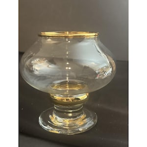 May include: A clear glass bowl with a gold rim and base. The bowl has a rounded shape and sits on a short, pedestal-style base. The gold accents add a touch of elegance to the design.