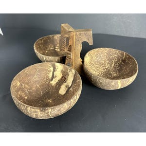 May include: Three brown coconut shell bowls with a wooden stand. The bowls are arranged in a triangular shape and are perfect for serving snacks or dips.