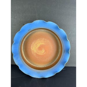 Könnte beinhalten: Ein Keramikteller mit einem wellenförmigen, hellblauen Rand und einer Mitte, die von Orange zu Gold übergeht. Der Teller hat ein handgefertigtes Aussehen mit sichtbarer Textur und leichten Unvollkommenheiten.