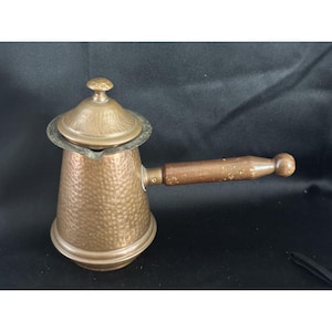 May include: A hammered copper coffee pot with a wooden handle and a lid. The pot has a rounded body and a spout. The handle is attached to the side of the pot.
