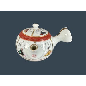 May include: A white ceramic teapot with a round body, a red and gold band, and a curved handle. The teapot is decorated with painted figures and calligraphy. The lid has a small white knob. The spout is centered on the body.