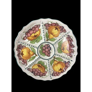 Pode incluir: Uma travessa de servir em cerâmica branca com seis secções, cada uma decorada com uma pera amarela e uvas roxas. A travessa tem uma borda ondulada e uma borda verde, perfeita para servir aperitivos ou lanches.