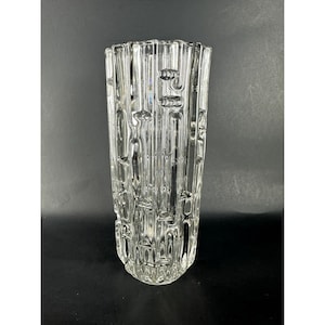 May include: A clear glass vase with a textured, ribbed design. The vase has a cylindrical shape and a wide opening.