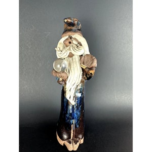 Könnte beinhalten: Eine Keramikfigur eines Zauberers mit langem weißem Bart, der eine blaue und braune Robe trägt und eine klare Glaskugel hält.