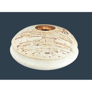 May include: A handcrafted, ceramic vessel with a unique, organic shape. The off-white exterior features intricate, brown, textured patterns. The top has a circular opening with a bronze-colored interior. This decorative piece is ideal for home decor.