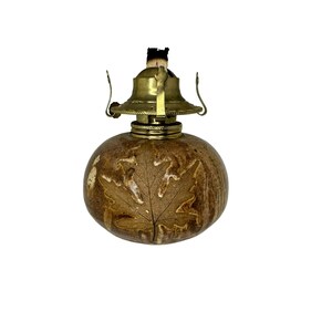May include: A brown ceramic oil lamp with a brass top and a leaf design. The lamp is lit and has a wick.