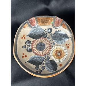 Op de afbeelding: Een ronde keramische schaal met een bloemenmotief. De schaal is beschilderd met zwarte, bruine, witte en oranje bloemen en bladeren. De schaal heeft een bruine rand.