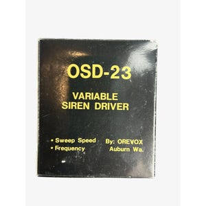 May include: A black rectangular box with yellow text that reads OSD-23 VARIABLE SIREN DRIVER. The text also includes Sweep Speed, Frequency, and By: OREVOX Auburn Wa. The surface of the box is glossy and shows minor signs of wear and light reflection.