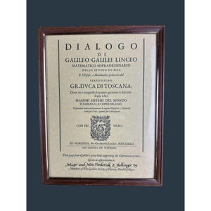 May include: A framed title page from Galileo's book, featuring Italian text and a detailed emblem. The frame is a dark brown, and the paper has a beige hue. The text includes the title "DIALOGO" and the names "GALILEO GALILEI LINCEO".