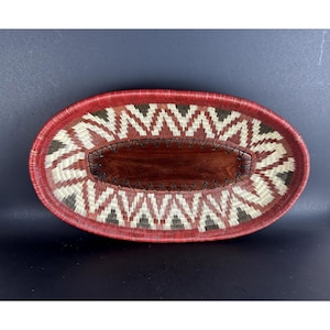 May include: Oval woven basket with a red rim and a geometric pattern in white, red, and black. The basket has a wooden base.