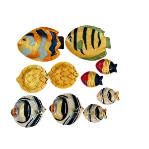 May include: A set of nine ceramic fish-shaped serving dishes. The dishes are painted in various colors, including yellow, blue, red, and green. The dishes are in different sizes and shapes, and some are paired together.