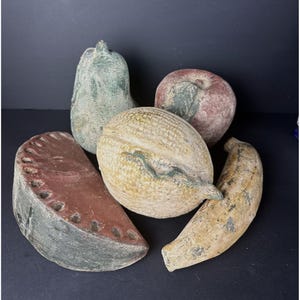 Puede incluir: Una colección de cinco esculturas de frutas de cerámica pintadas a mano. Las esculturas incluyen una pera, una manzana, un plátano, una rodaja de sandía y un melón. Las esculturas están pintadas en colores realistas y tienen una superficie texturizada.