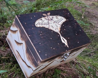 May include: A rectangular wooden box with a dark stained lid featuring a wood-burned luna moth and small dots. The sides of the box are light-colored wood with wood-burned mountain silhouettes and a silver-toned metal latch on the front.