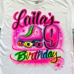 May include: White t-shirt with a pink roller skate and the number 9 in pink with the words "Laila's Birthday" in rainbow colors.