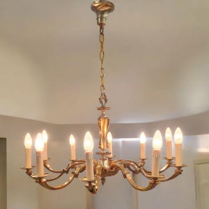May include: A gold-toned chandelier with 10 candle-style light bulbs. The chandelier has a curved, ornate design and is hanging from a chain.