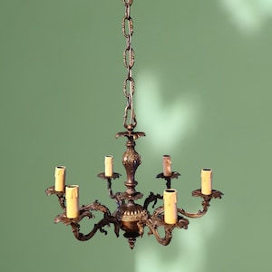 May include: A bronze chandelier with five candle-style light bulbs hanging from a chain against a green wall.
