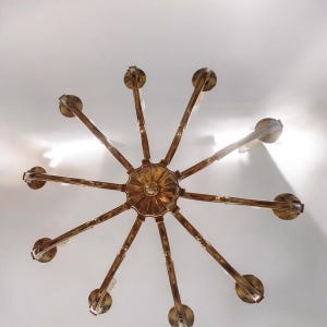 May include: A gold-toned chandelier with eight arms extending from a central circular fixture. The chandelier has a starburst design and is viewed from below.