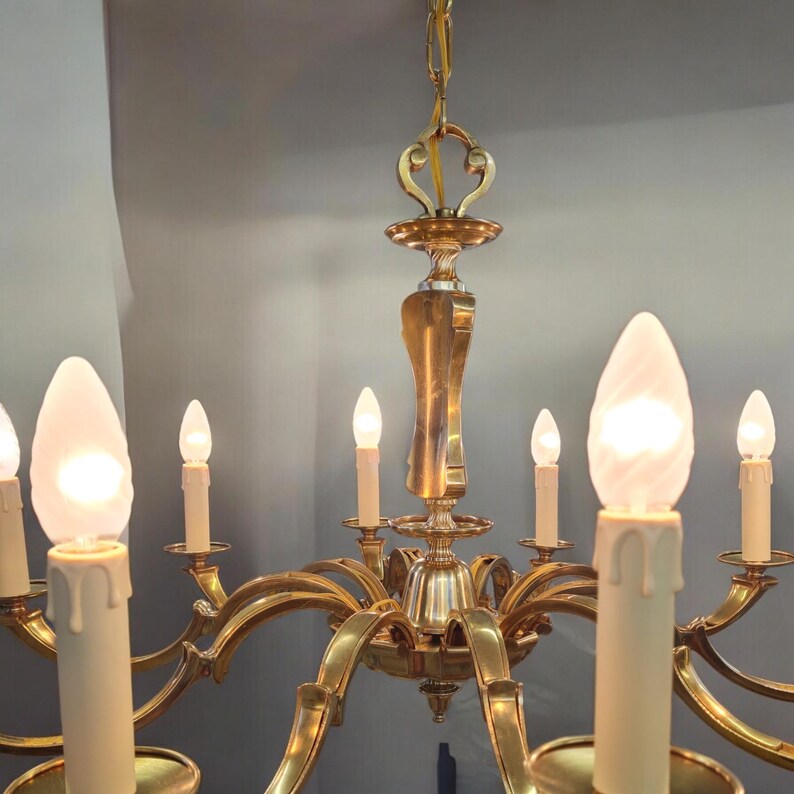 May include: A gold-toned brass chandelier with eight candle-style light bulbs. The chandelier has a decorative, ornate design with curved arms and a central finial.