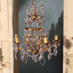 May include: A gold chandelier with crystal drops and five candle holders. The chandelier has a delicate, ornate design with a floral motif.