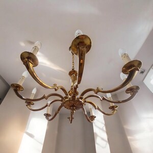May include: A gold-toned chandelier with eight arms and eight light bulbs. The chandelier has a decorative design with scrolls and curves.