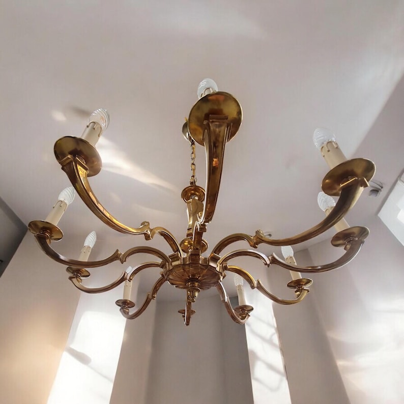 May include: A gold-toned chandelier with eight arms and eight light bulbs. The chandelier has a decorative design with scrolls and curves.