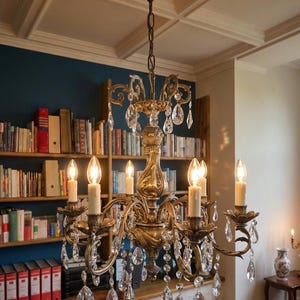May include: A multi-armed brass chandelier featuring ornate scrollwork and numerous hanging clear crystal teardrop prisms. The fixture includes six candle-style light bulbs with off-white sleeves, suspended from the ceiling by a matching metal chain.